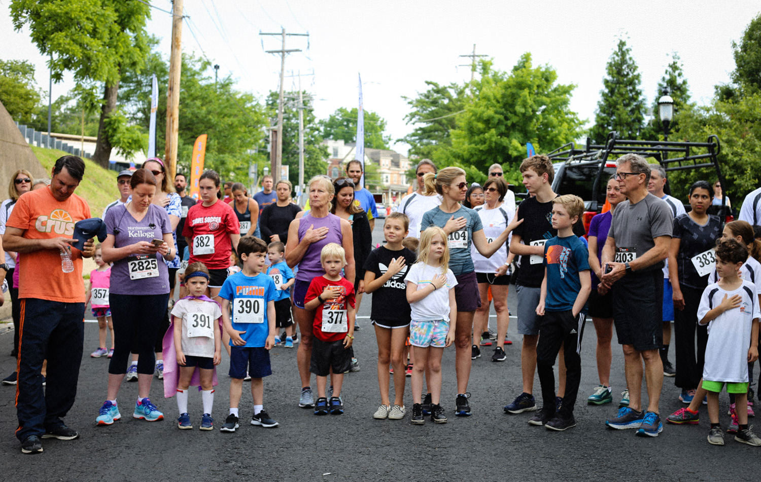 Runners and families standing with hands over their hearts for the national anthem before the BCRR Twilight 5K