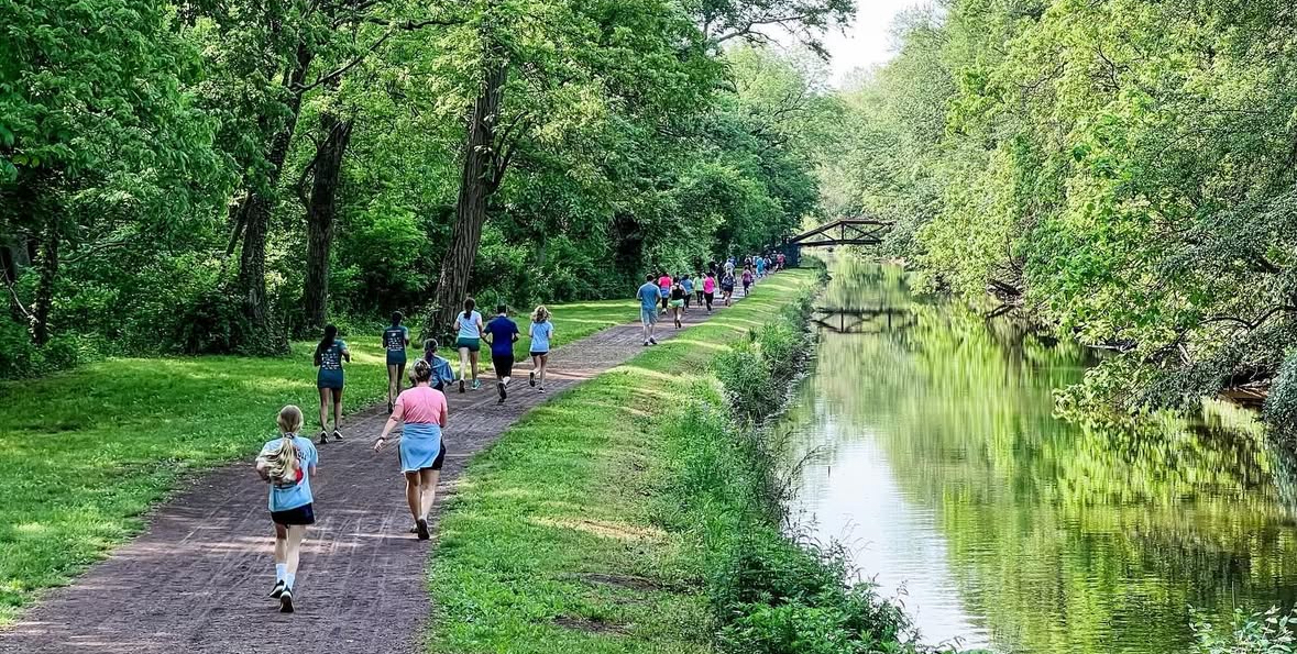 A pack of runners racing along the tree-lined Yardley 5K course near the Delaware Canal